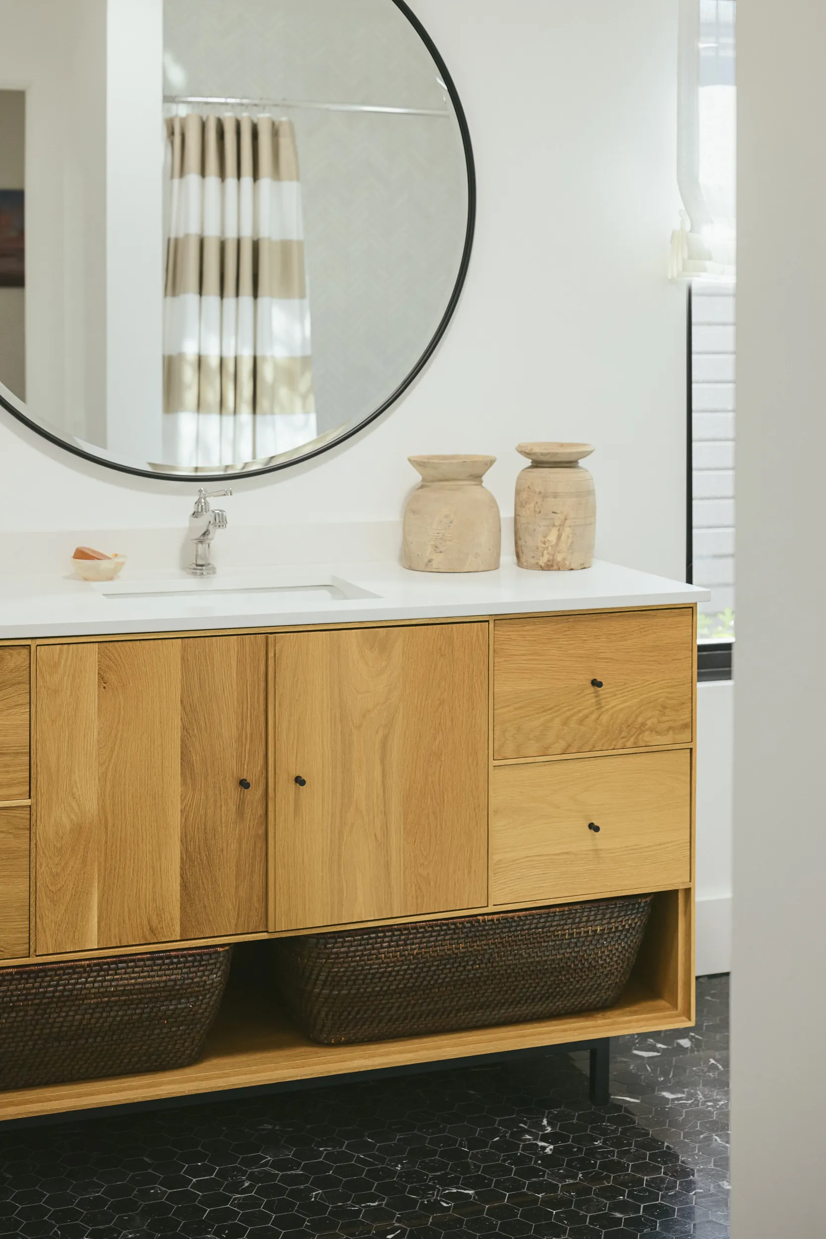 Floating oak wood bathroom vanity with white countertop, round black mirror, and black hexagonal floor tiles House Rupert interior design Santa Barbara and Montecito