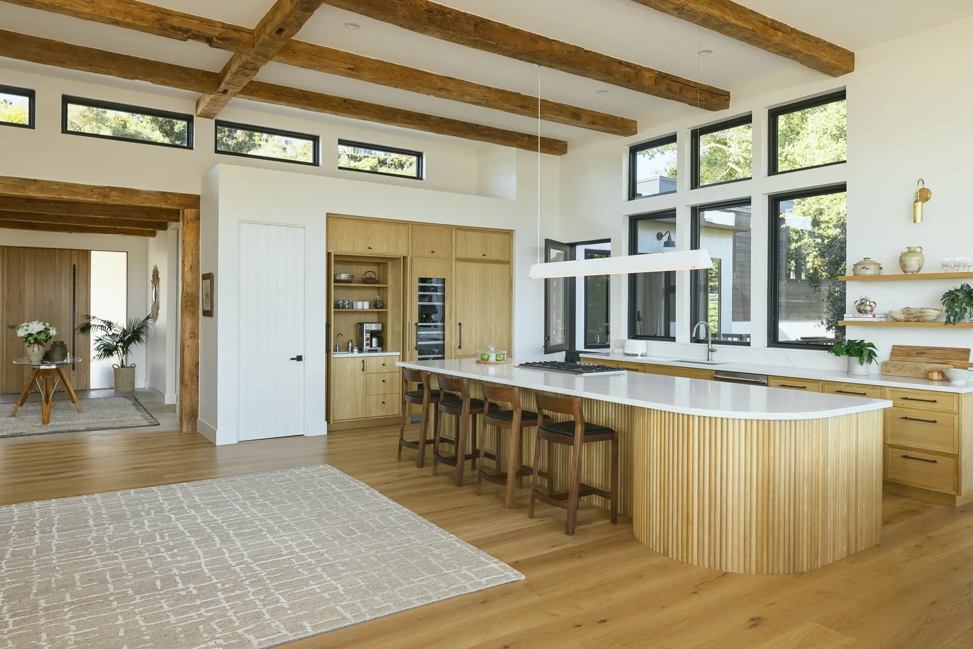 Modern kitchen featuring exposed wood ceiling beams, light oak cabinetry, white quartz countertops and large windows House Rupert interior design Santa Barbara and Montecito