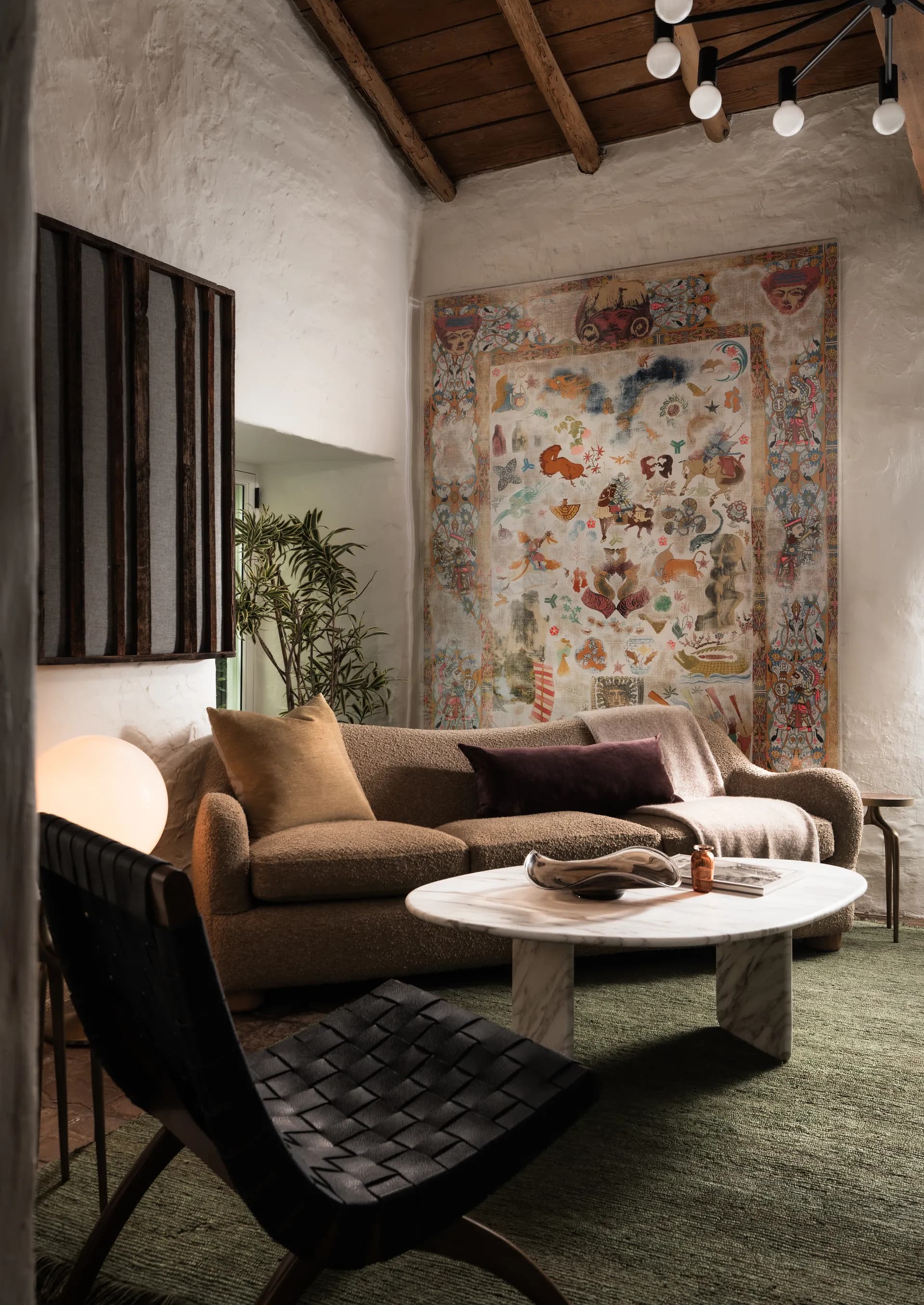 Rustic living room featuring exposed wood ceiling beams, neutral sectional sofa, round coffee table, and vibrant wall tapestry House Rupert interior design Santa Barbara and Montecito