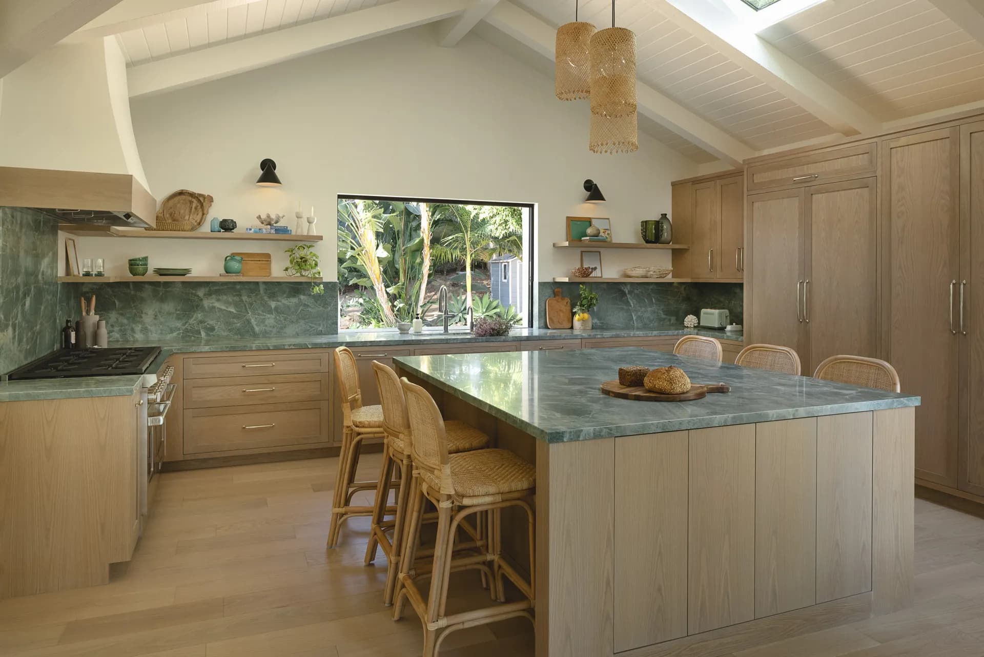 Modern coastal kitchen featuring natural wood cabinetry, green marble countertops and backsplash, woven pendant lights, and tropical garden views House Rupert interior design Santa Barbara and Montecito