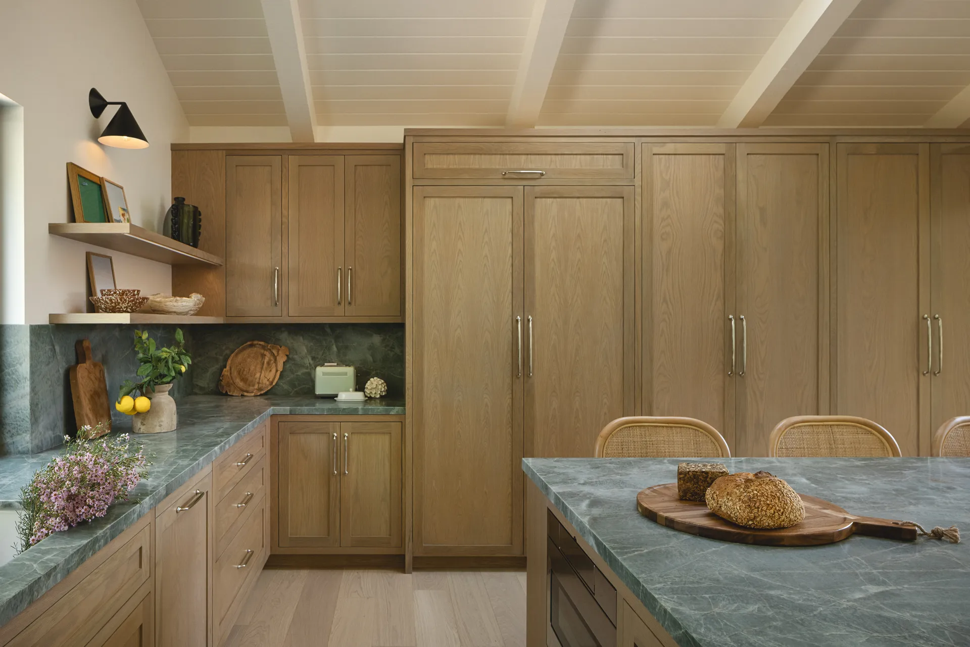 Natural oak kitchen cabinets with green marble countertops and island, exposed wood beam ceiling, woven dining chairs, House Rupert interior design Santa Barbara and Montecito