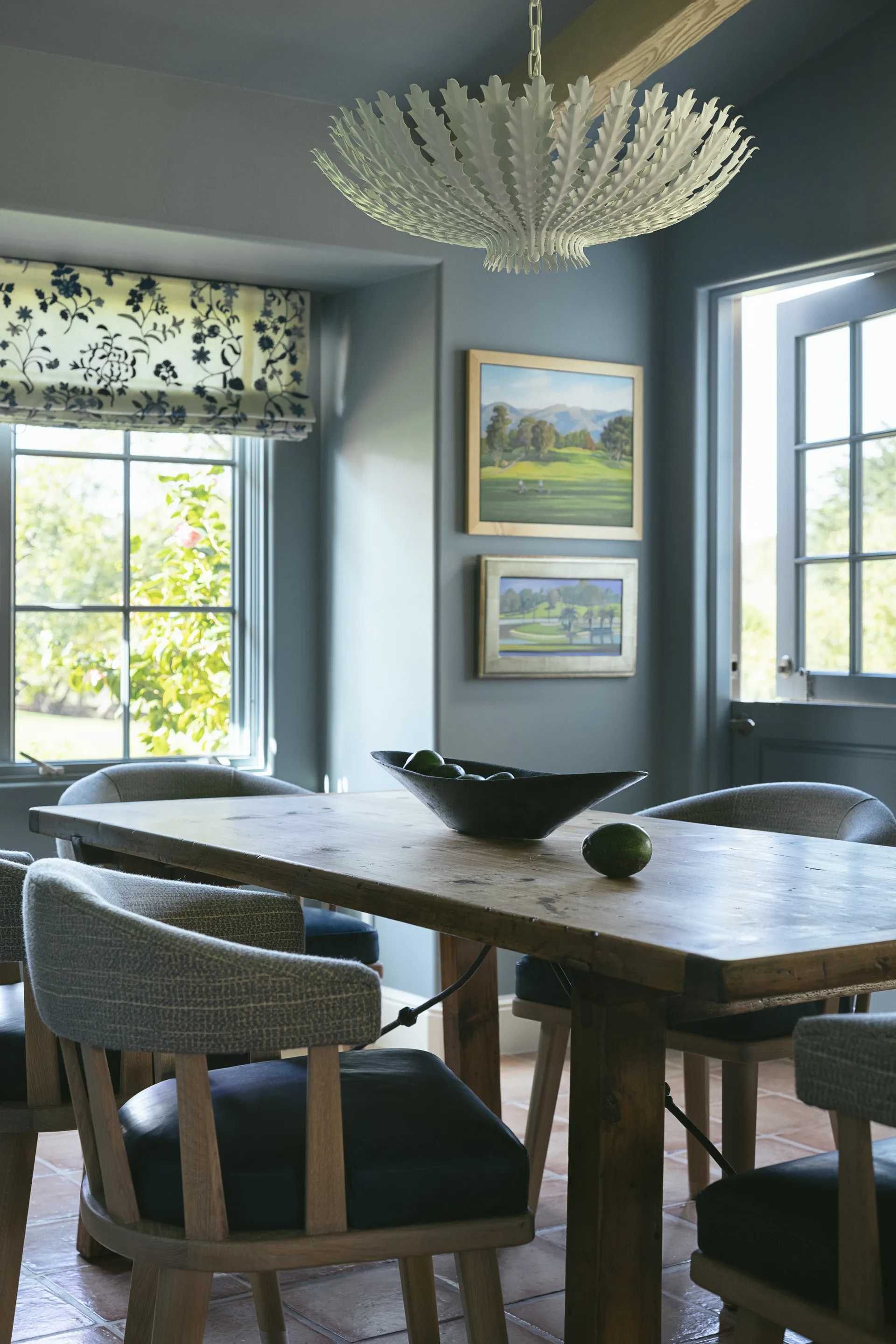 Blue dining room with rustic wood table, upholstered chairs, white coral chandelier, and landscape artwork House Rupert interior design Santa Barbara and Montecito