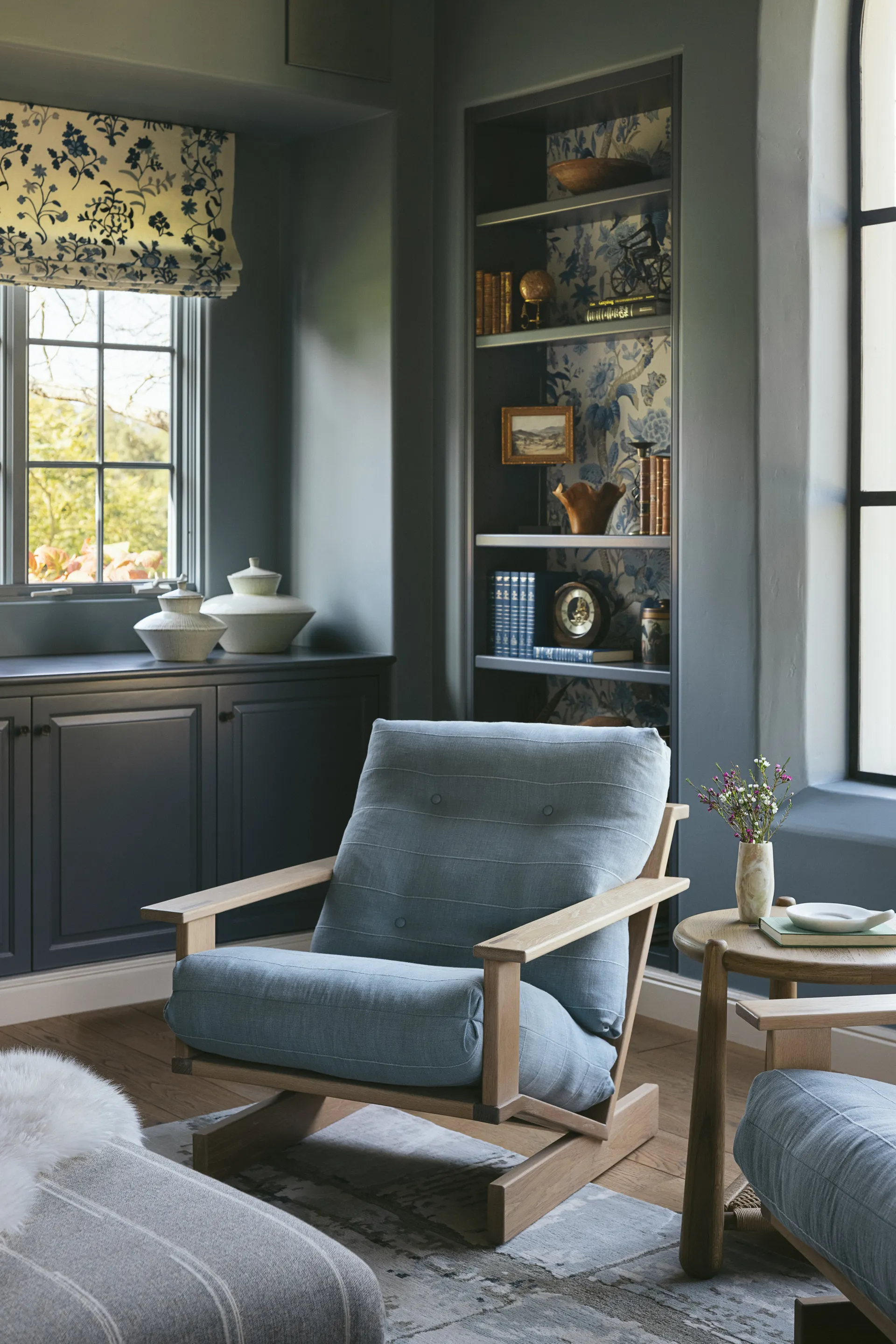 Sage green painted built-in bookshelf with blue floral wallpaper backing, linen armchair, and coordinating roman shade House Rupert interior design Santa Barbara and Montecito