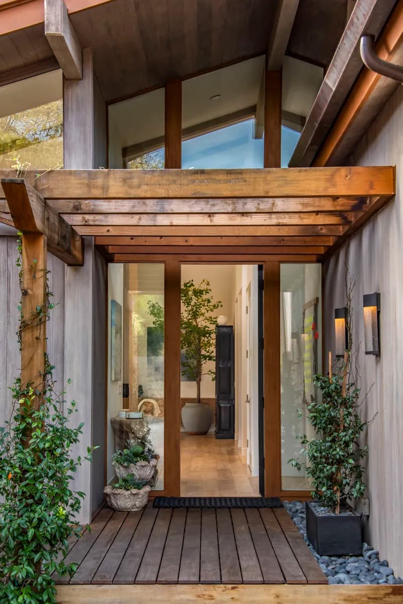 Modern home entry with glass doors, exposed wood beam pergola, concrete walls, and landscaped planters House Rupert interior design Santa Barbara and Montecito