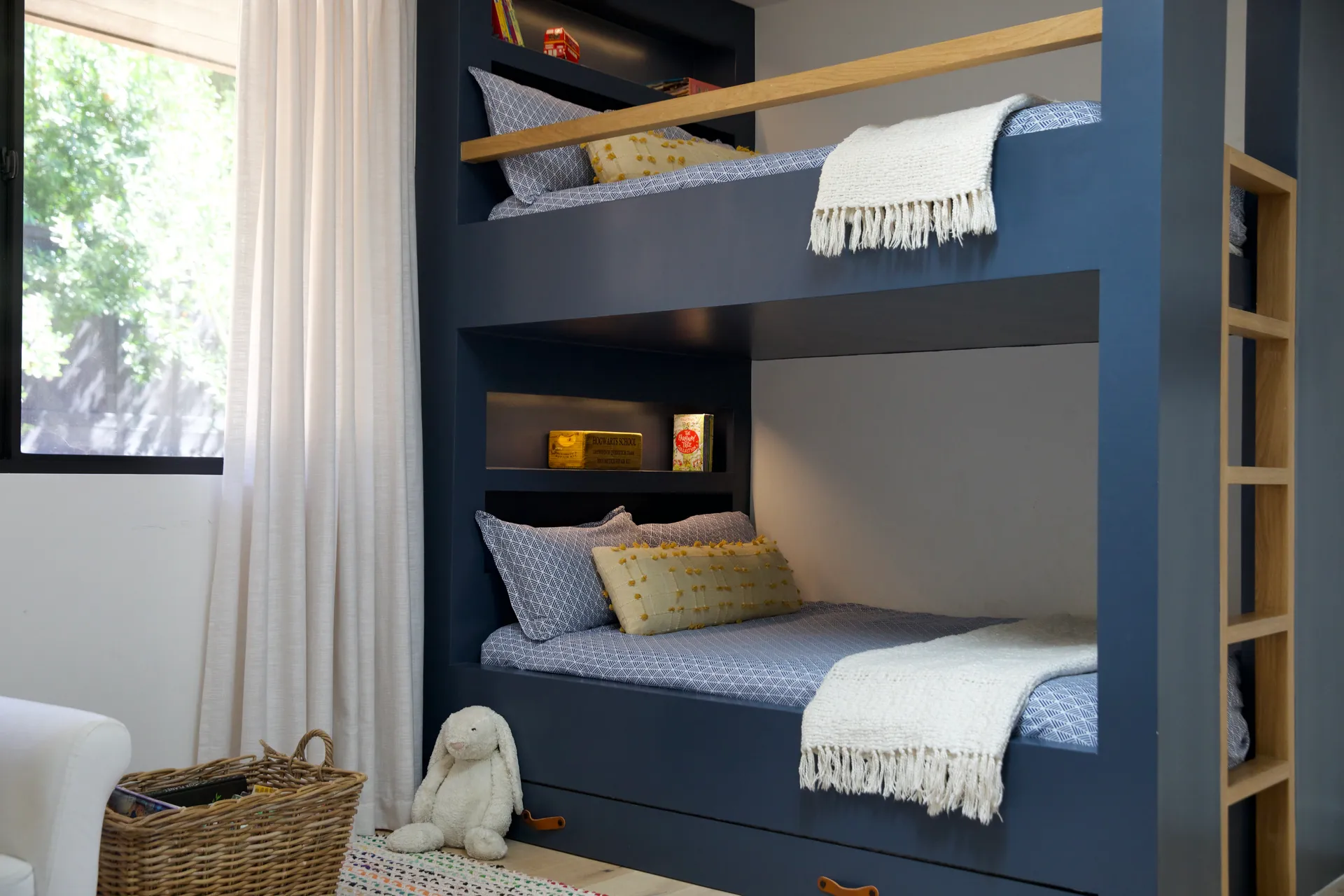 Navy blue built-in bunk beds with natural wood ladder, white fringe throws, and wicker storage basket House Rupert interior design Santa Barbara and Montecito