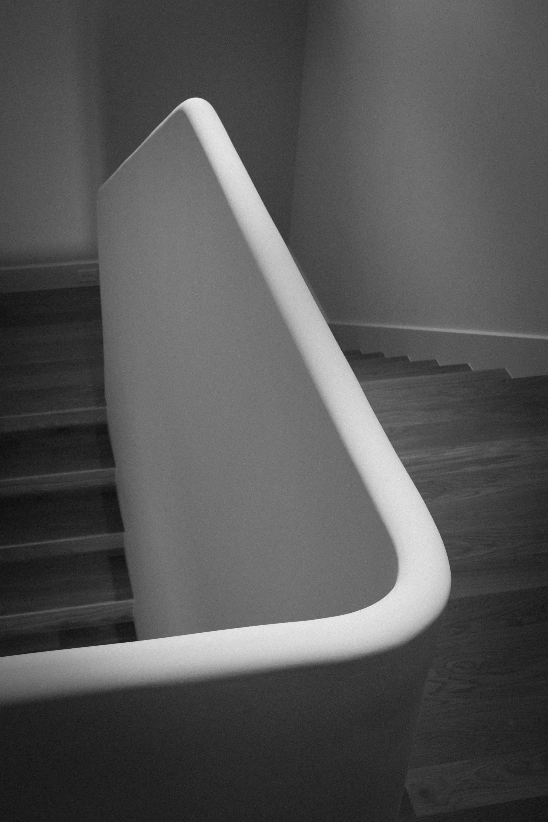 Modern curved white upholstered chair positioned beside natural wood staircase in minimalist interior space House Rupert interior design Santa Barbara and Montecito