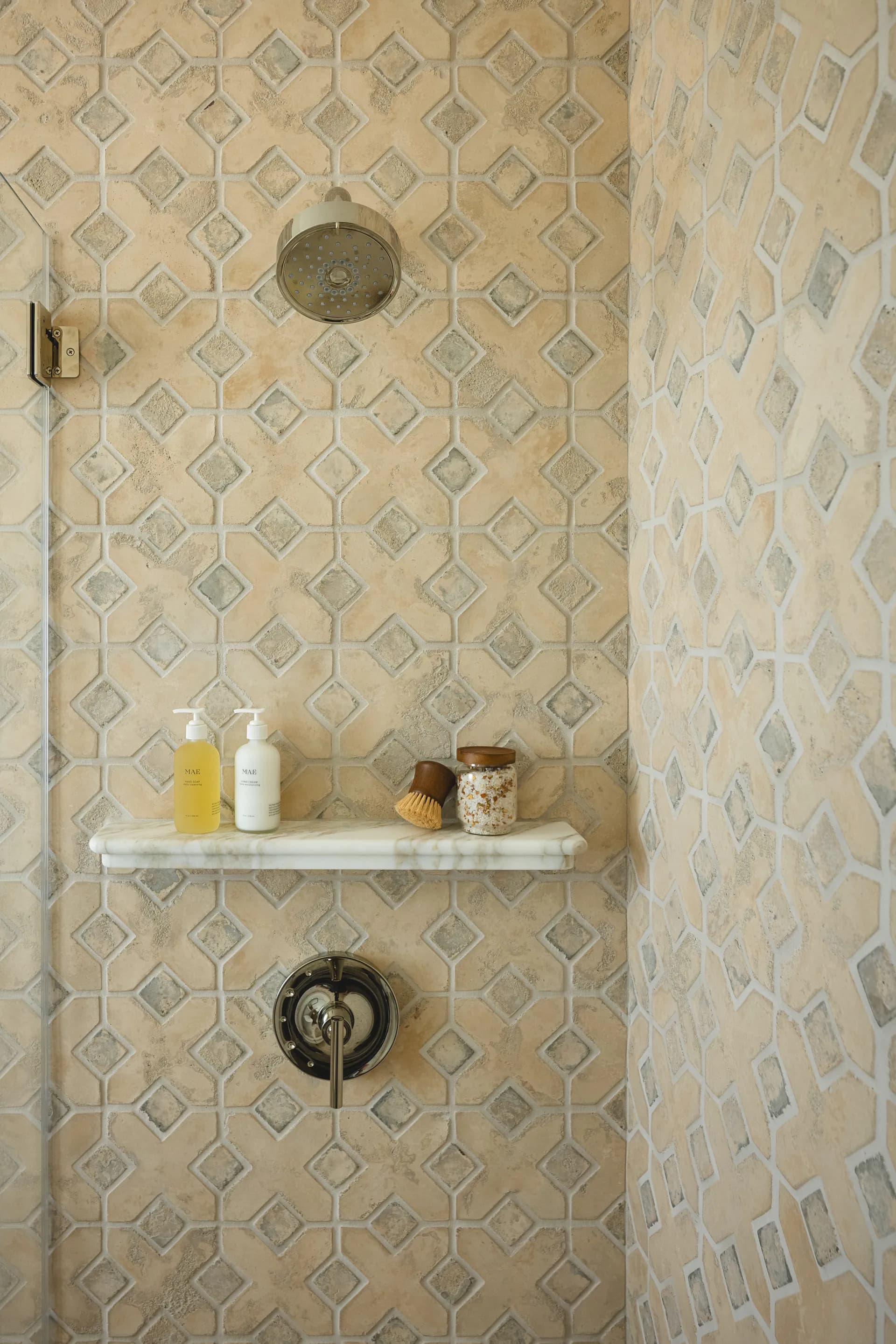 Elegant shower featuring geometric stone tile pattern with marble built-in shelf and brass fixtures House Rupert interior design Santa Barbara and Montecito