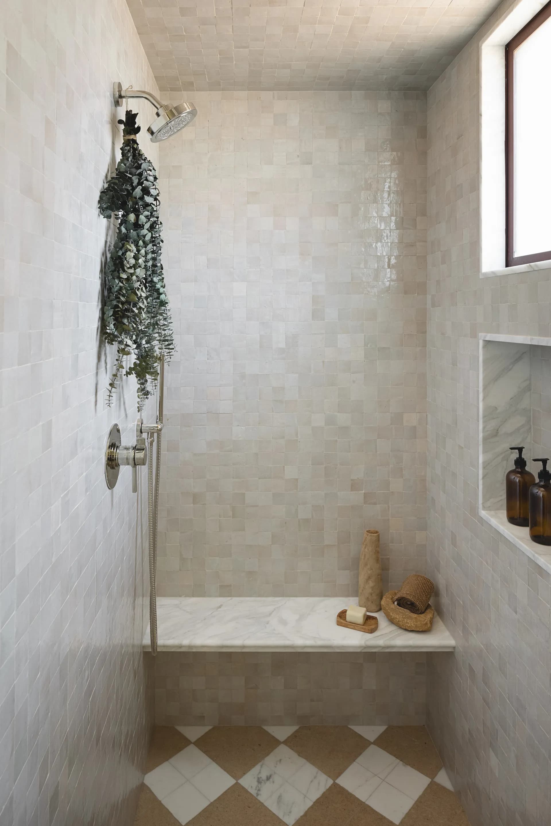 Luxury spa-style shower featuring white marble mosaic tiles, eucalyptus bundle, built-in bench with natural accessories, and checkered floor - House Rupert interior design Santa Barbara and Montecito