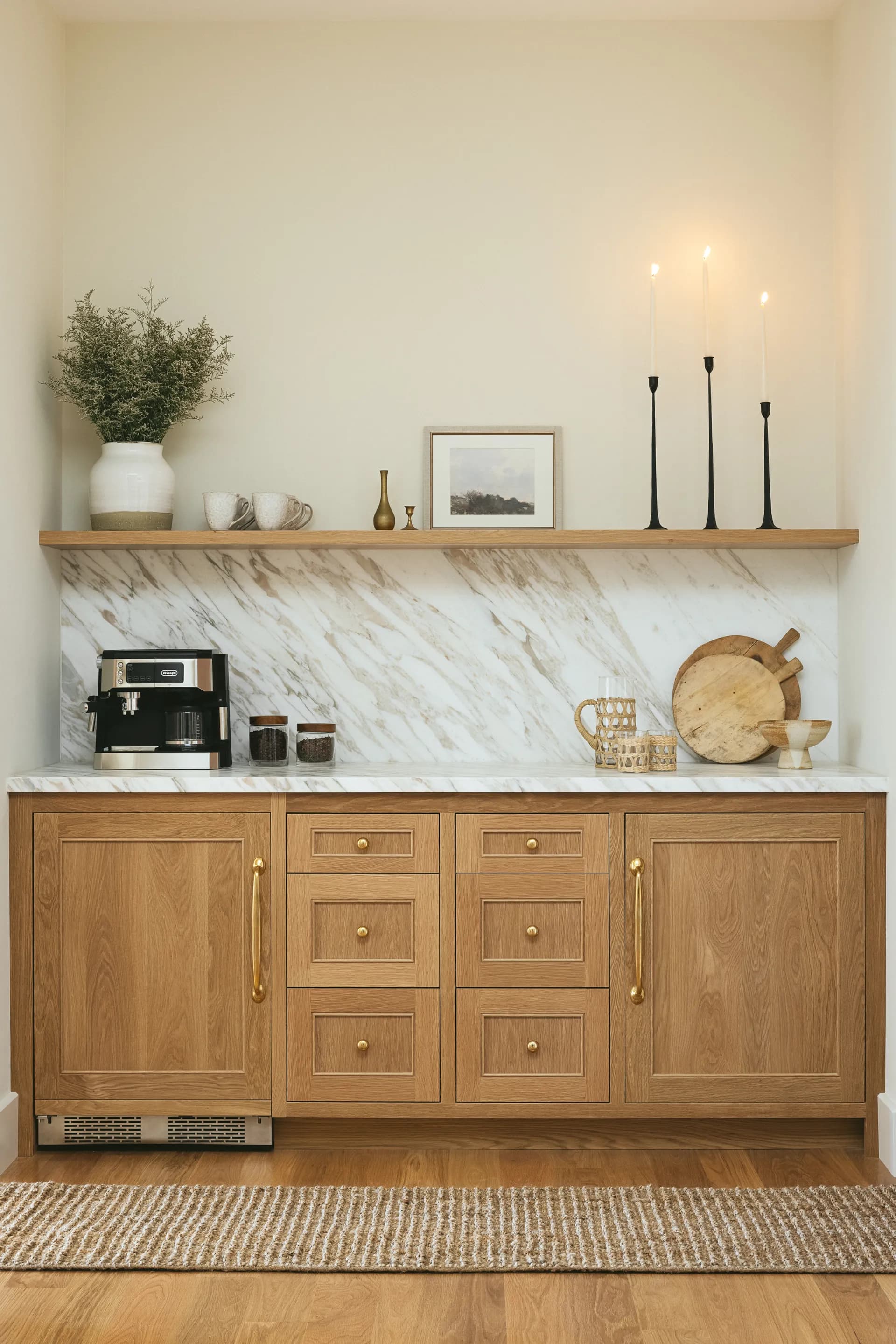 Modern kitchen featuring oak wood cabinetry with brass hardware, white marble backsplash and countertops, floating wood shelf with decorative objects, House Rupert interior design Santa Barbara and Montecito