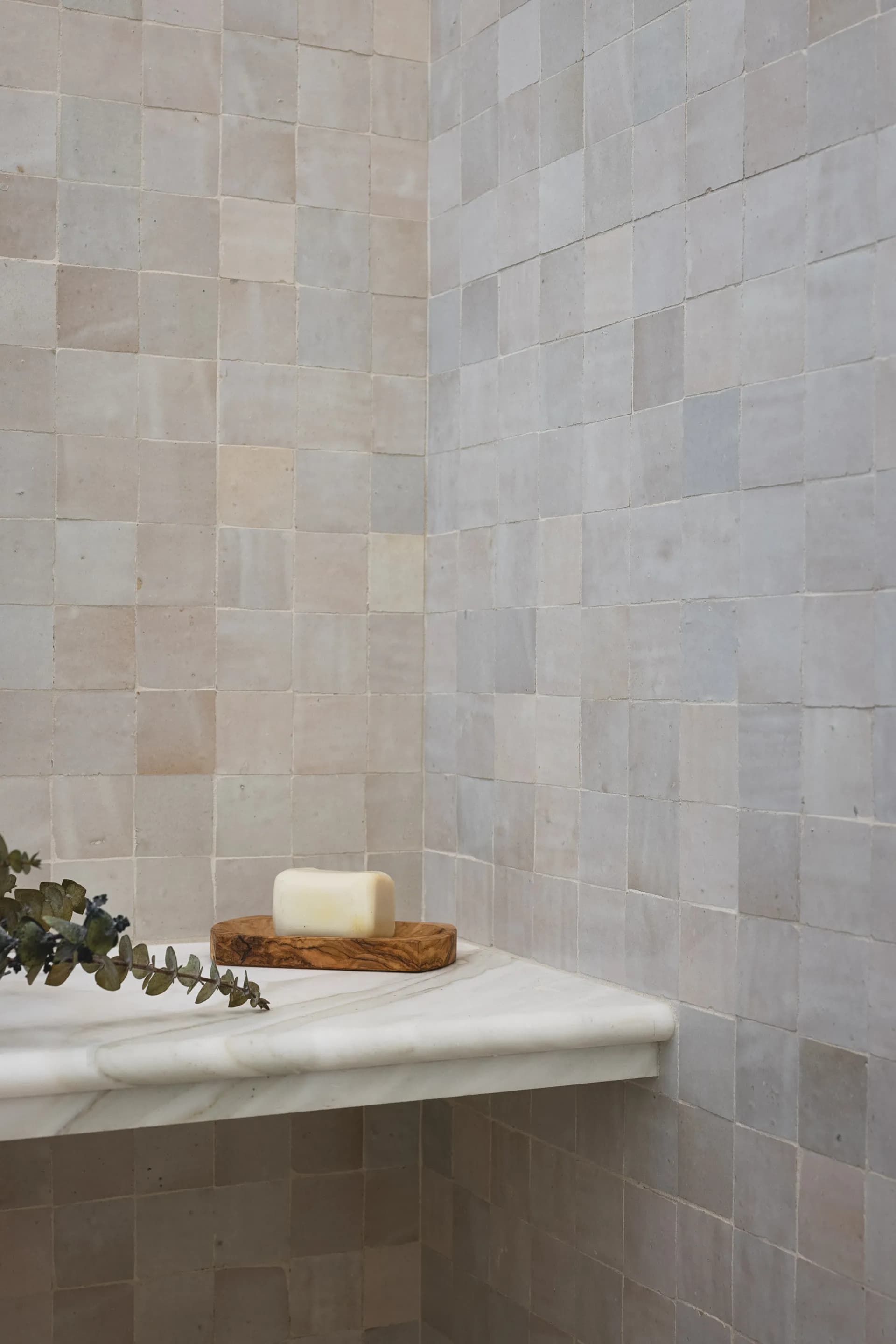 Natural stone tile bathroom corner with white marble floating shelf, wooden soap dish, eucalyptus sprig and bar soap House Rupert interior design Santa Barbara and Montecito