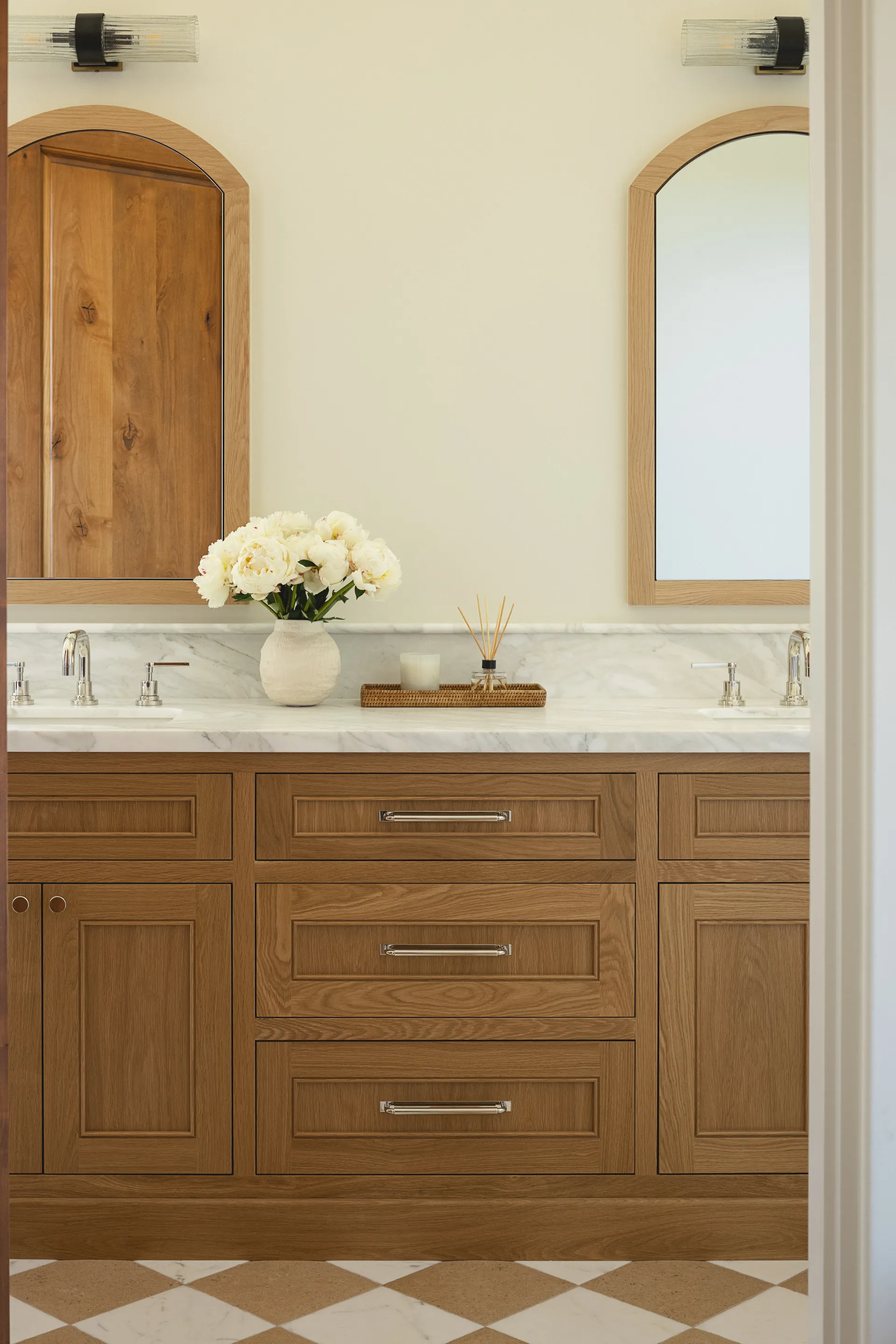 Custom natural wood bathroom vanity with arched mirrors, white marble countertop, and geometric floor tiles House Rupert interior design Santa Barbara and Montecito