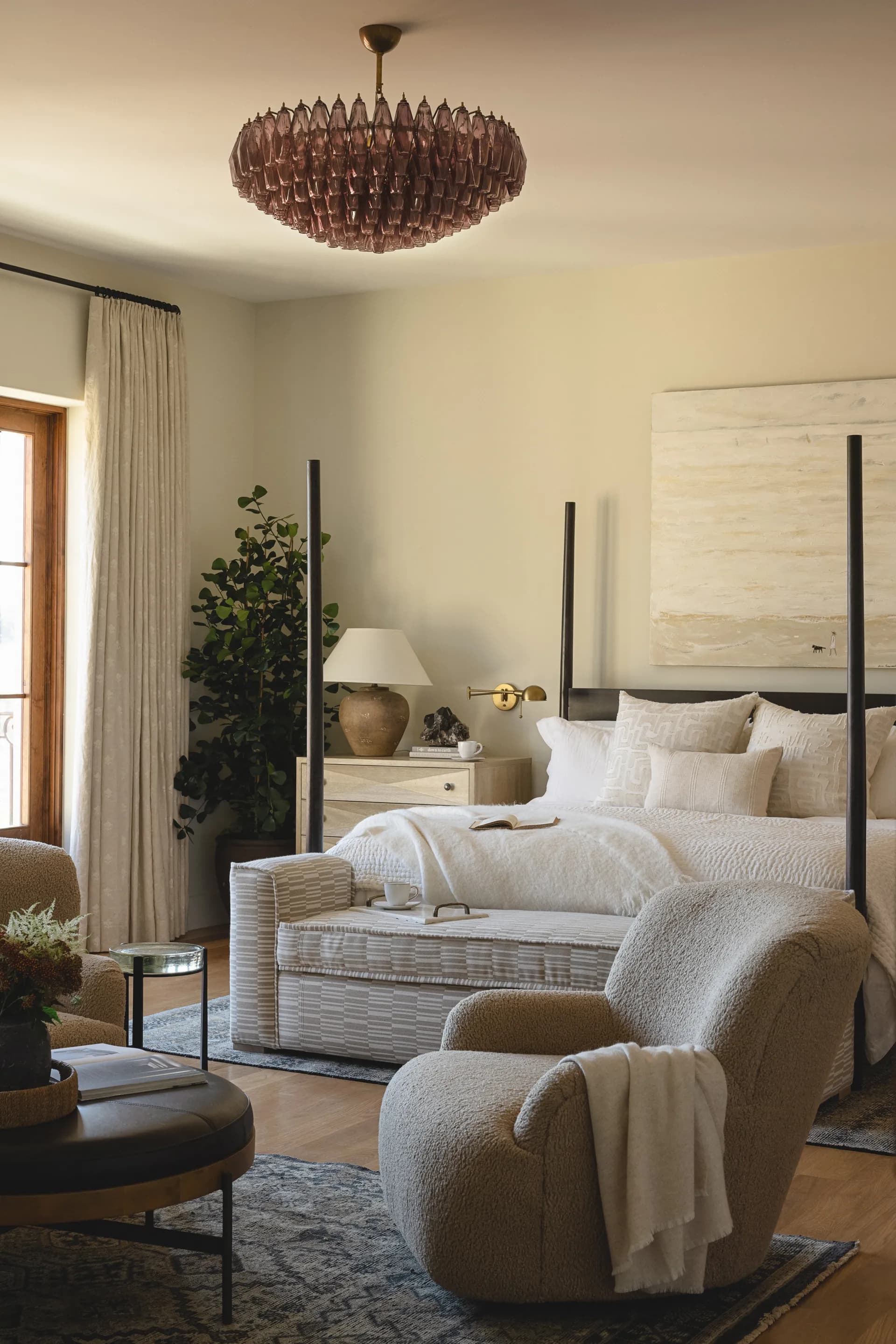 Neutral bedroom featuring black four-poster bed, pink glass chandelier, cream armchair, and textured bench House Rupert interior design Santa Barbara and Montecito