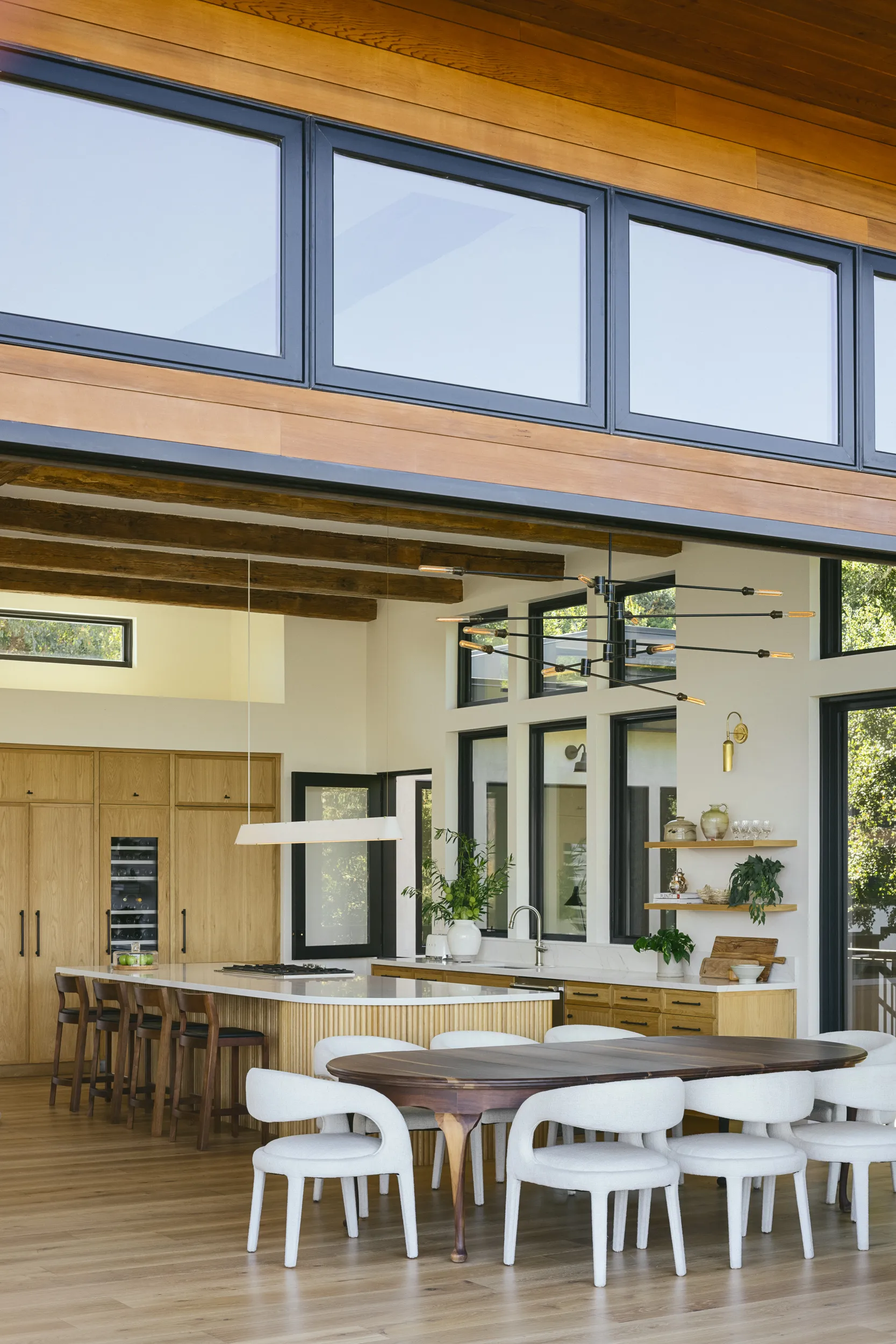 Modern open-plan kitchen and dining area with exposed wood beams, white marble island, natural wood cabinetry, and white curved dining chairs House Rupert interior design Santa Barbara and Montecito