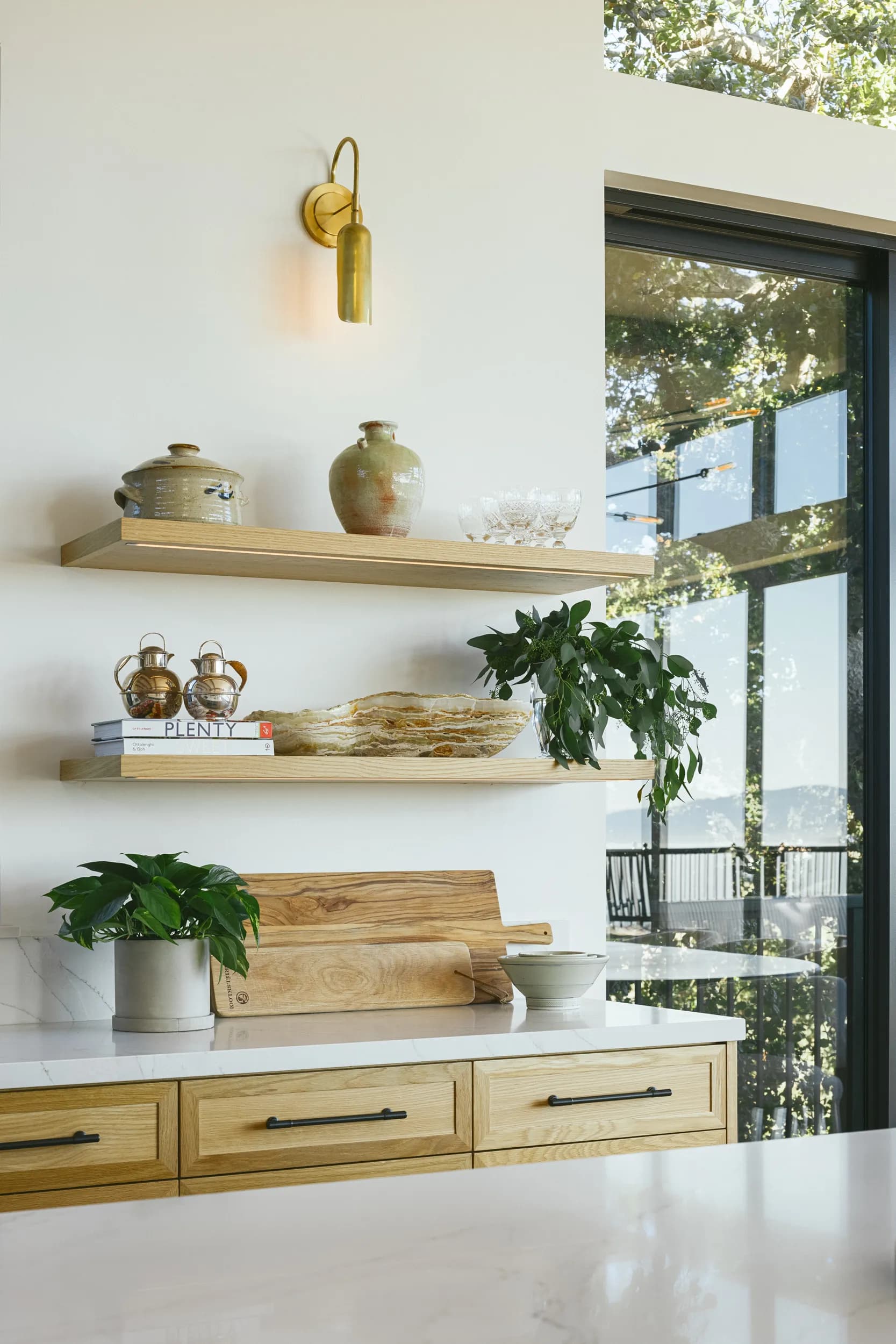 Modern kitchen featuring floating wood shelves, brass wall sconce, white quartz countertops, and natural wood cabinetry House Rupert interior design Santa Barbara and Montecito