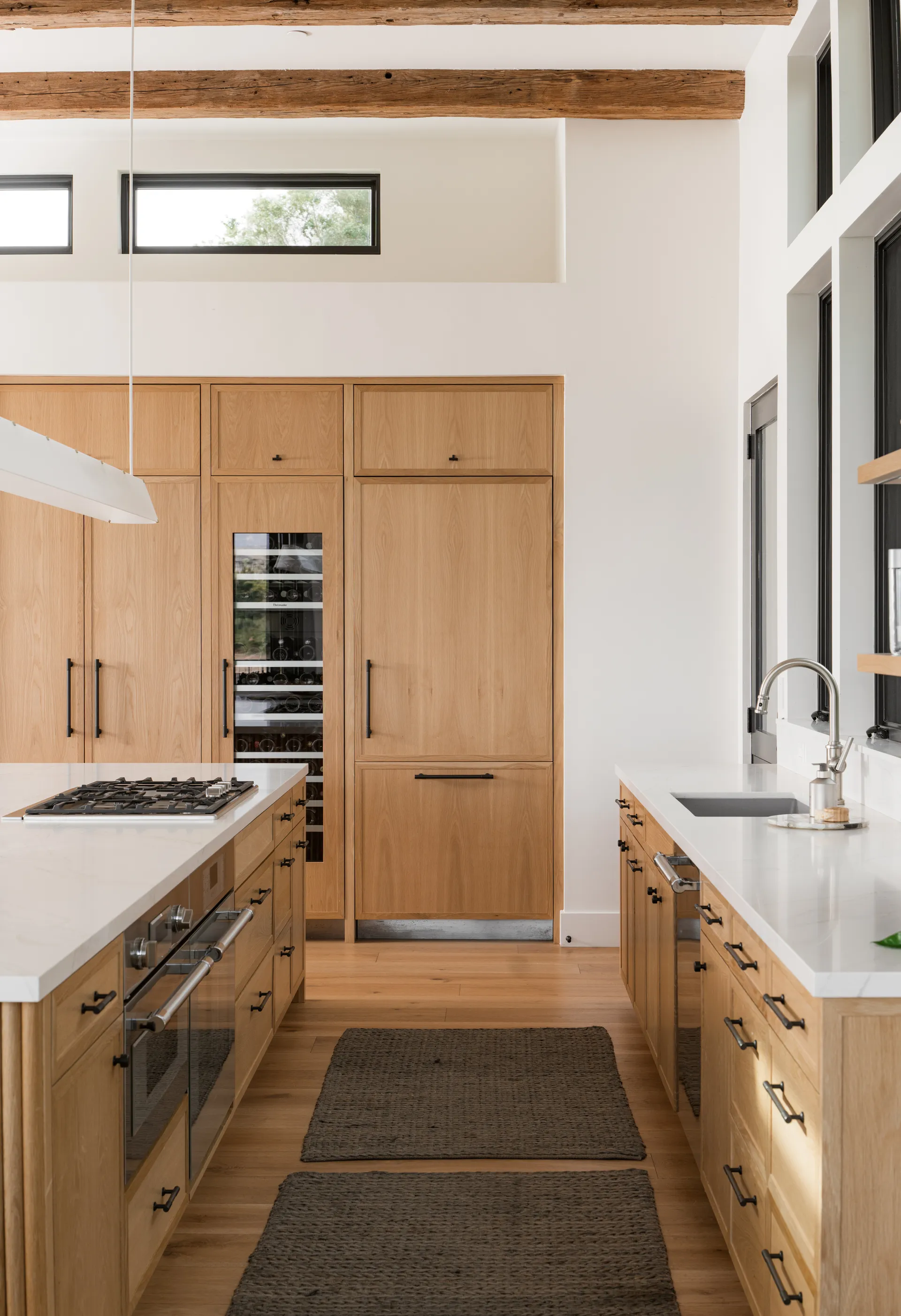 Modern kitchen featuring light wood cabinets, white quartz countertops, exposed ceiling beams, and black hardware House Rupert interior design Santa Barbara and Montecito