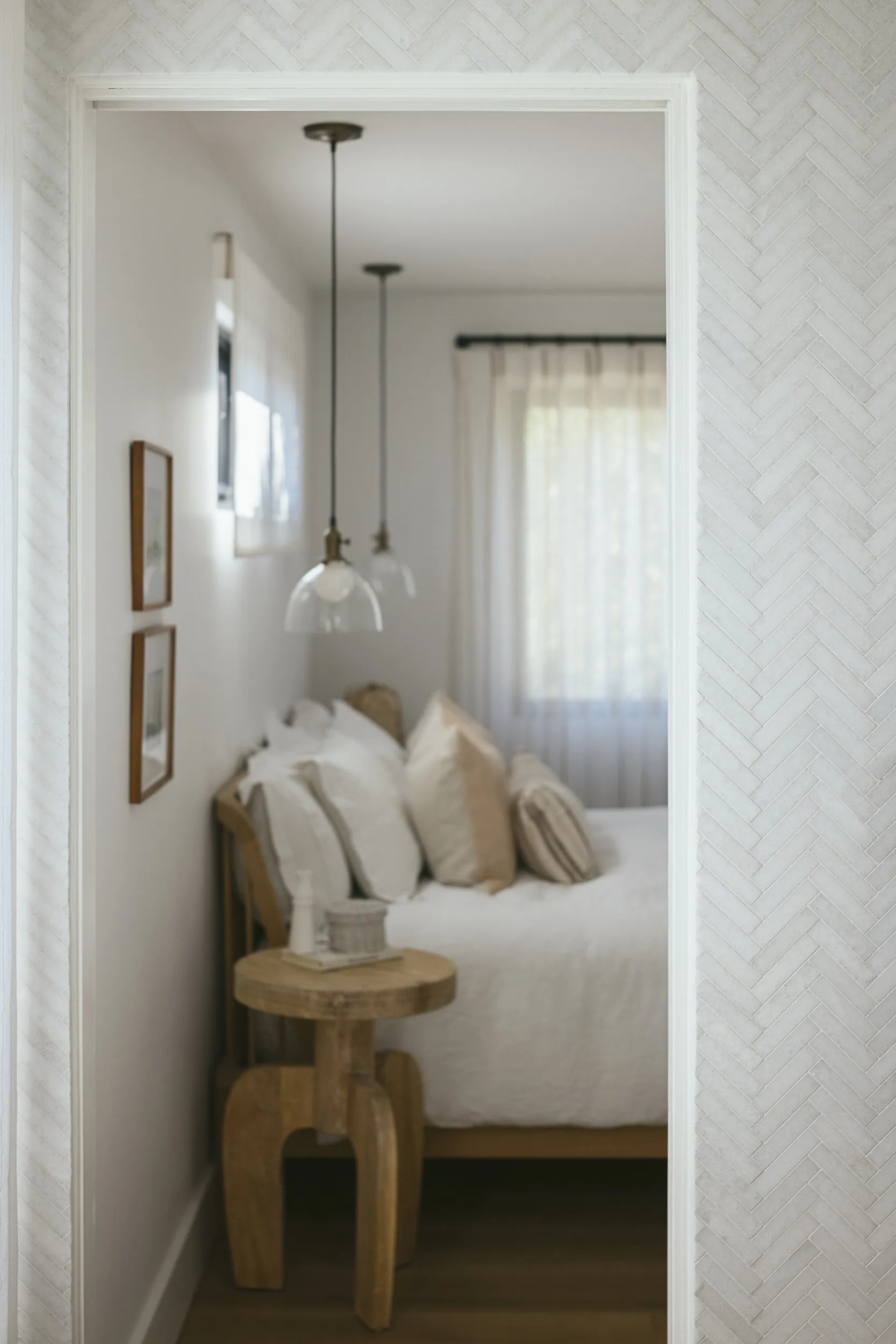 Serene bedroom featuring white herringbone wallpaper, glass globe pendant lights, neutral linen bedding and natural wood stool House Rupert interior design Santa Barbara and Montecito