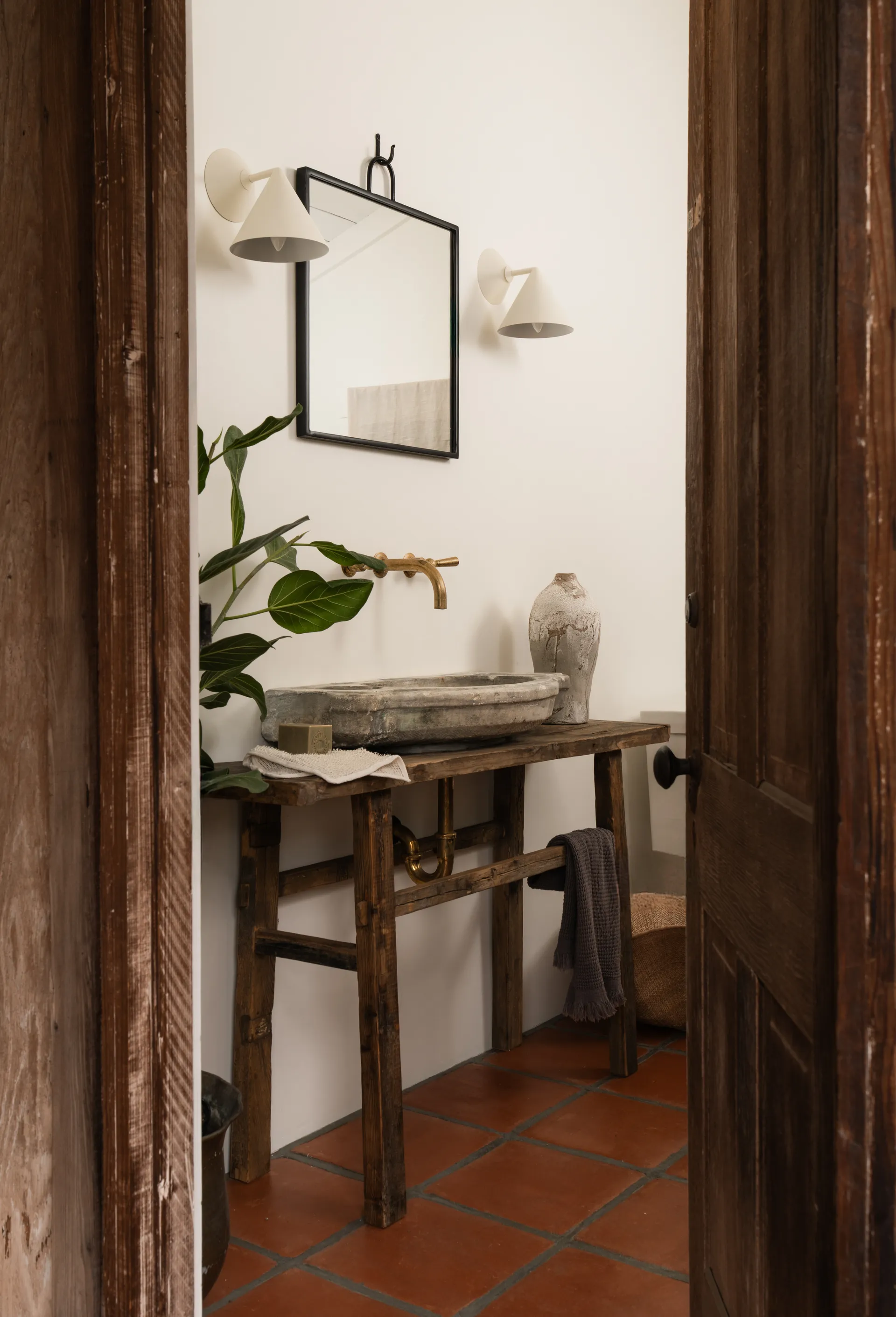 Rustic powder room featuring reclaimed wood vanity with stone vessel sink, brass wall-mount faucet, and terracotta tile flooring House Rupert interior design Santa Barbara and Montecito