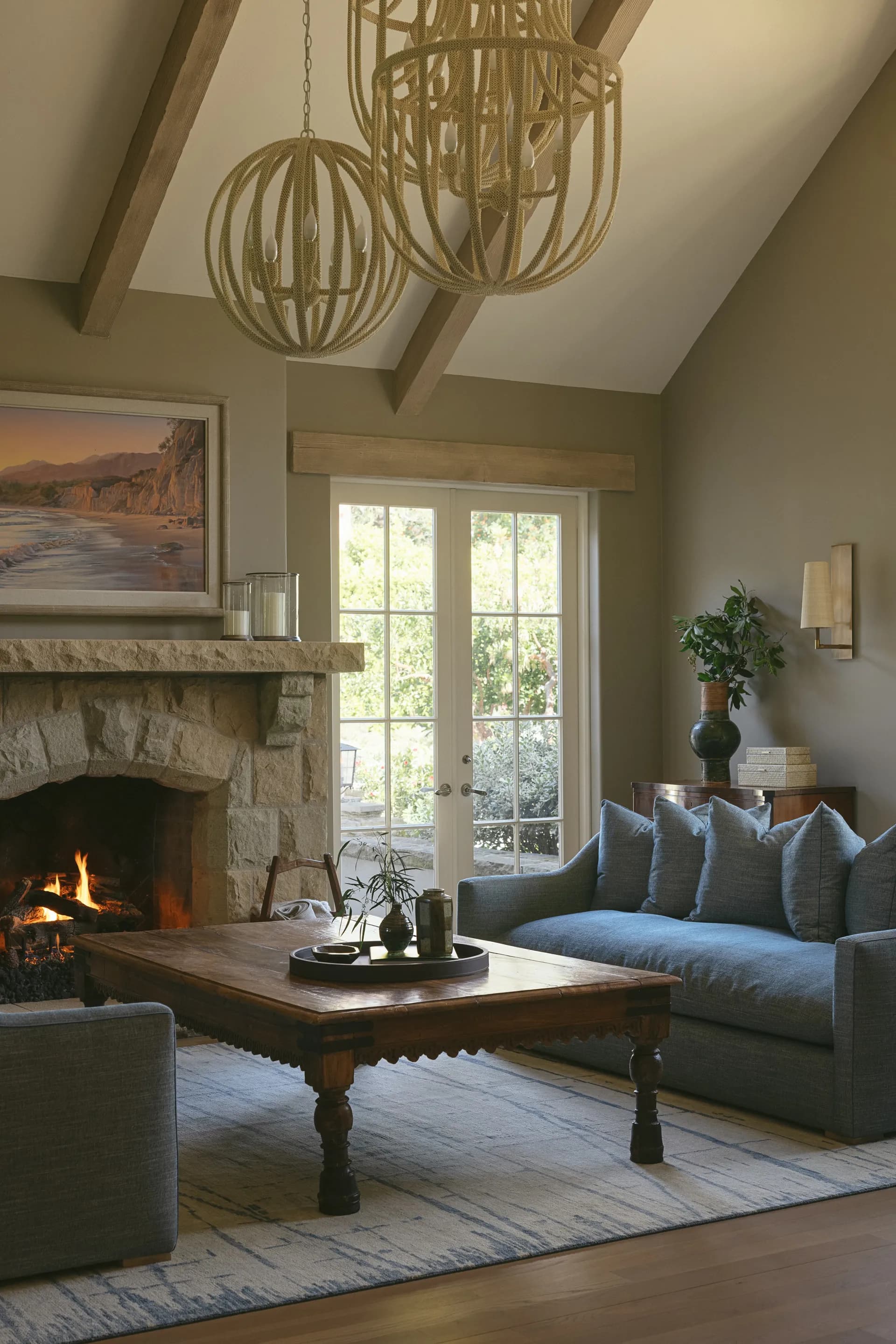 Rustic living room with stone fireplace, blue sectional sofa, wooden coffee table, and vaulted ceiling beams House Rupert interior design Santa Barbara and Montecito