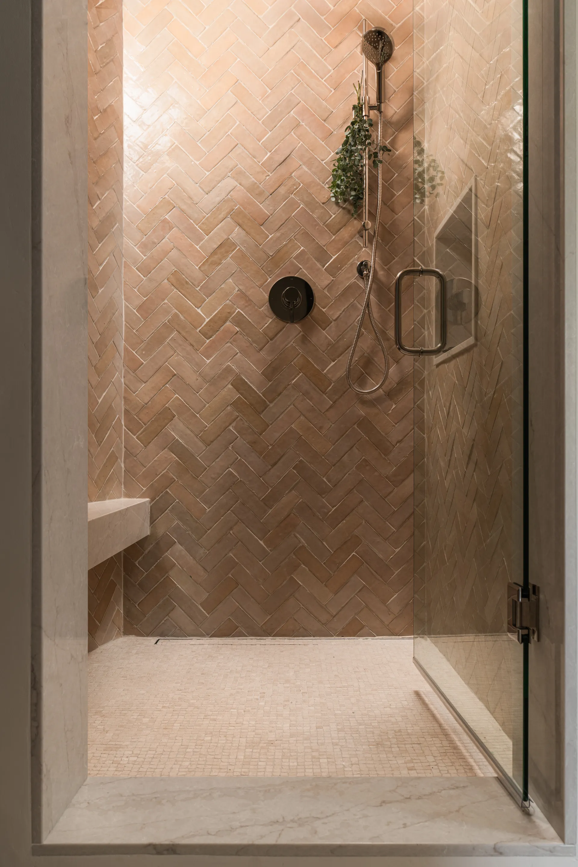 Luxury walk-in shower with cream herringbone tile walls, brass fixtures, glass door, and built-in bench seating House Rupert interior design Santa Barbara and Montecito