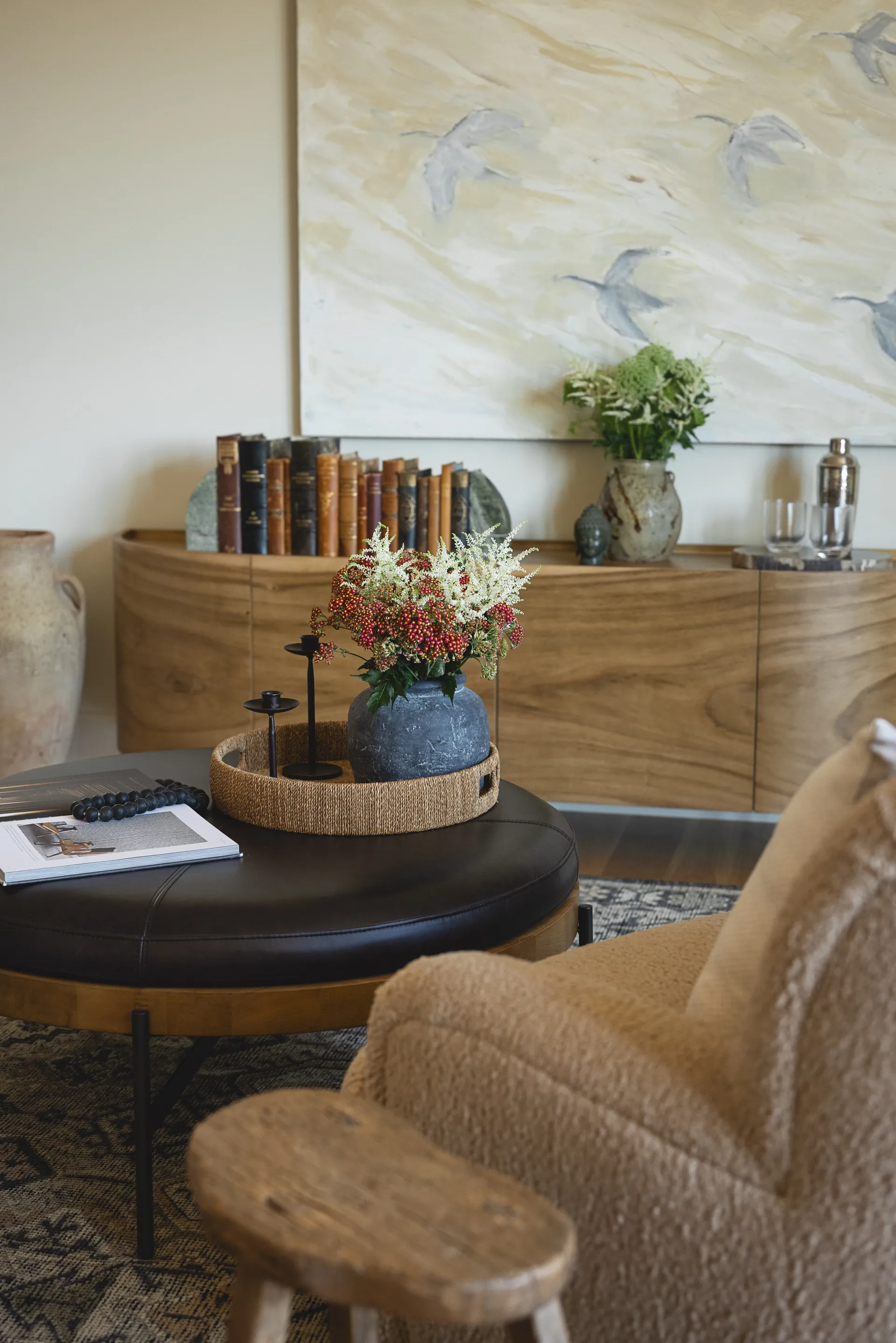 Modern living room featuring walnut wood credenza with books, round black leather coffee table, and textured beige armchair, House Rupert interior design Santa Barbara and Montecito